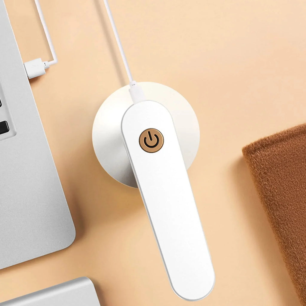 USB-powered white handheld gadget with power button on beige desk, next to laptop and towel