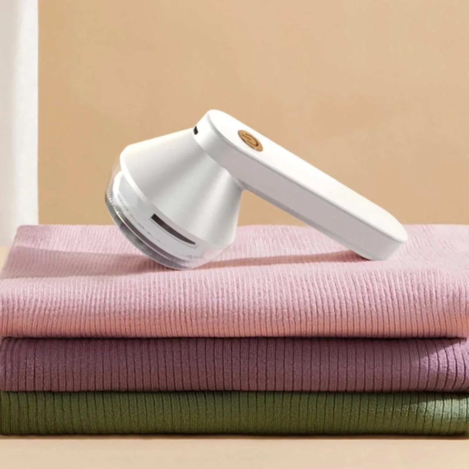 Electric fabric lint remover resting on folded ribbed sweaters, home gadget for clothes care