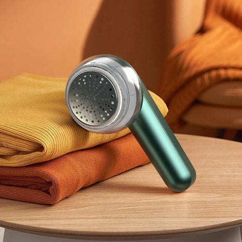Fabric shaver lint remover on a table with folded sweaters, home gadget for clothing care